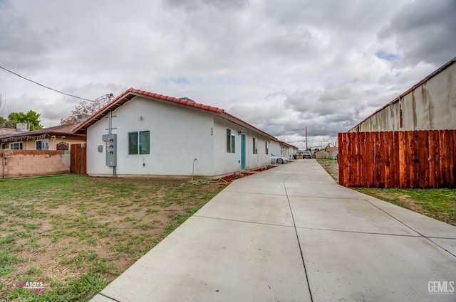 view of property exterior with stucco siding, a tile roof, a yard, and fence