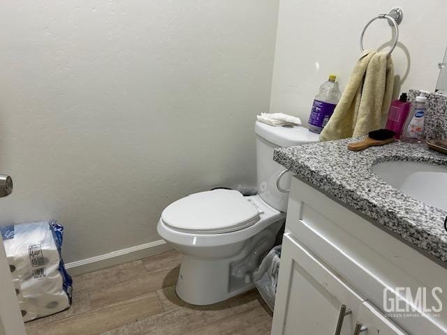 half bathroom with baseboards, toilet, wood finished floors, and vanity