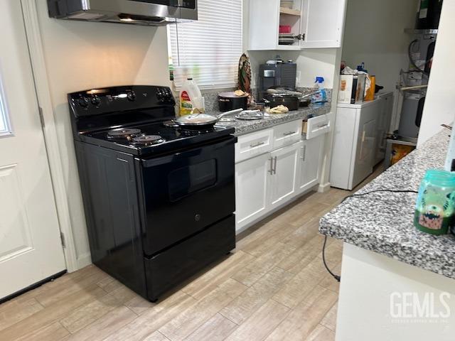 kitchen with light wood finished floors, washer / dryer, white cabinetry, and black / electric stove