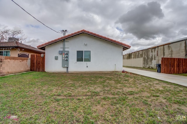 rear view of property with fence, a lawn, and stucco siding