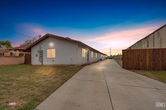 view of property exterior with a tile roof, fence, a lawn, and stucco siding