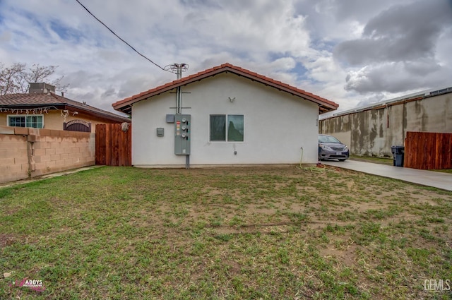 back of property with fence, stucco siding, concrete driveway, a tiled roof, and a lawn