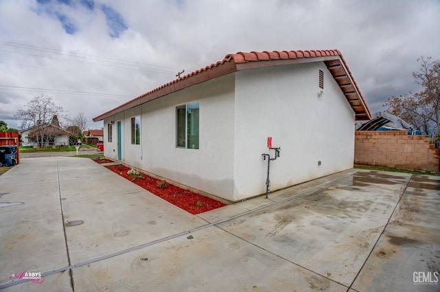 view of property exterior featuring a patio, concrete driveway, fence, and stucco siding