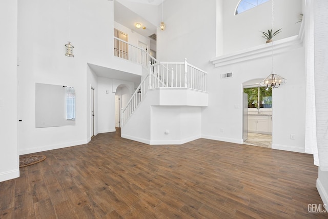 unfurnished living room featuring a notable chandelier, dark hardwood / wood-style flooring, and a towering ceiling