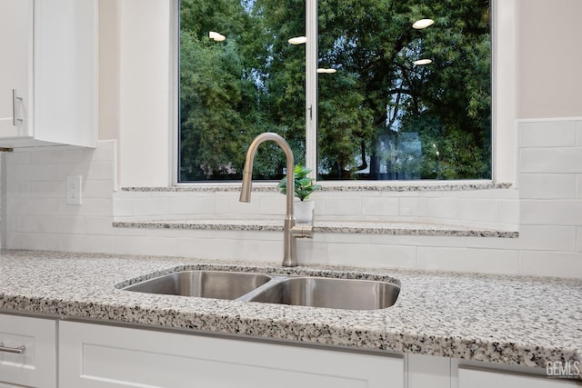 interior details featuring tasteful backsplash, white cabinetry, sink, and light stone countertops