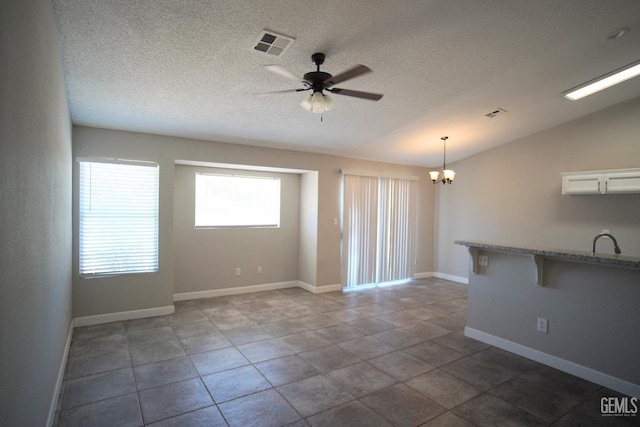 tiled empty room with baseboards, visible vents, vaulted ceiling, a textured ceiling, and ceiling fan with notable chandelier