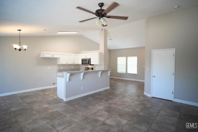 kitchen with light stone counters, white cabinetry, stainless steel microwave, a kitchen bar, and pendant lighting