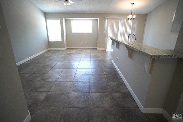 interior space featuring baseboards, a textured ceiling, decorative light fixtures, and a kitchen breakfast bar