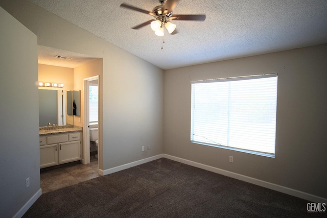 unfurnished bedroom featuring a textured ceiling, ensuite bathroom, baseboards, vaulted ceiling, and dark colored carpet