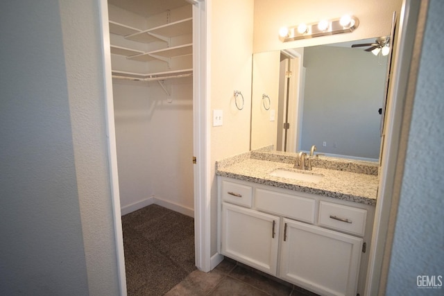 bathroom with baseboards, ceiling fan, tile patterned flooring, a walk in closet, and vanity