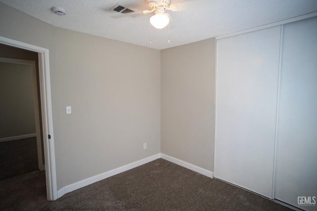 spare room featuring a textured ceiling, ceiling fan, visible vents, baseboards, and dark carpet