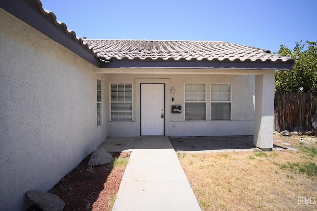 entrance to property with a tiled roof, fence, and stucco siding