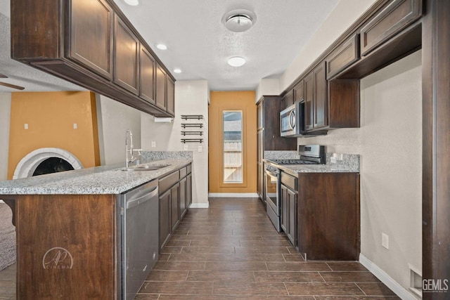 kitchen featuring stainless steel appliances, sink, dark brown cabinetry, and light stone counters