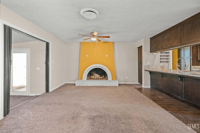 unfurnished living room featuring a fireplace, sink, dark colored carpet, ceiling fan, and a textured ceiling