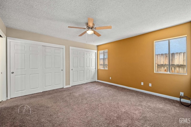 unfurnished bedroom with ceiling fan, two closets, a textured ceiling, and carpet