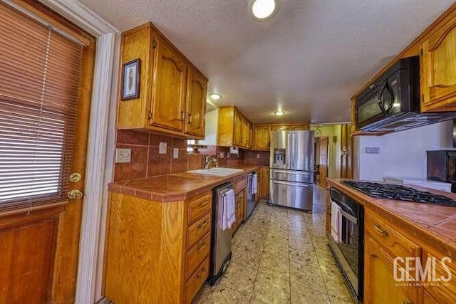 kitchen featuring black appliances, tile countertops, brown cabinetry, a textured ceiling, and a sink