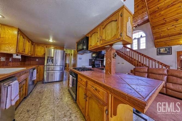 kitchen with a sink, stainless steel appliances, tile counters, brown cabinets, and backsplash