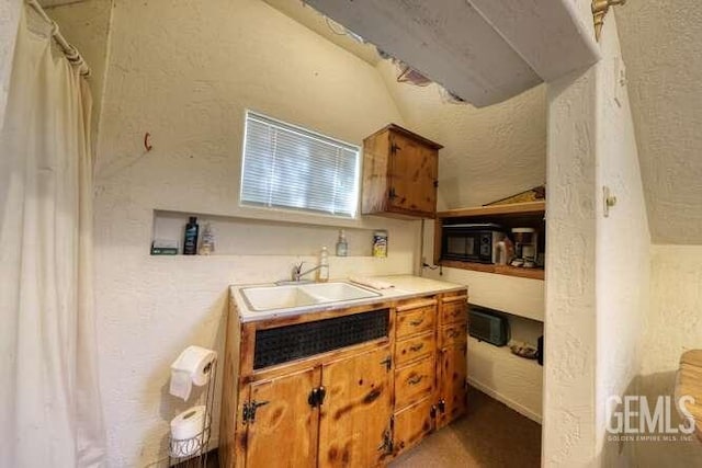 kitchen with brown cabinets, a sink, black microwave, light countertops, and a textured wall