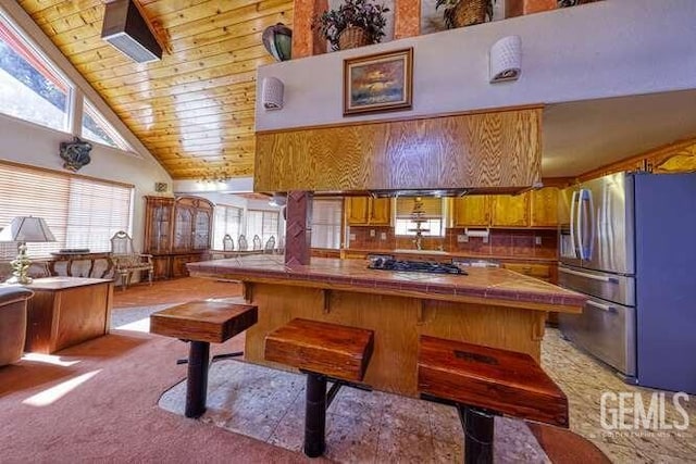 kitchen featuring high vaulted ceiling, appliances with stainless steel finishes, brown cabinetry, light colored carpet, and tile counters