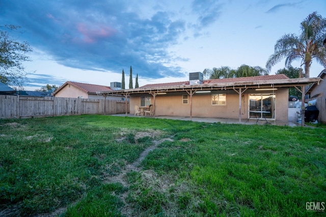 rear view of house featuring central air condition unit, stucco siding, a lawn, fence, and a patio area