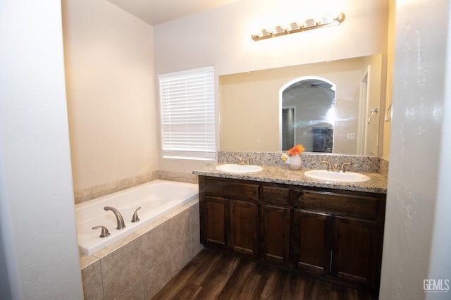 bathroom with hardwood / wood-style floors, vanity, and tiled bath