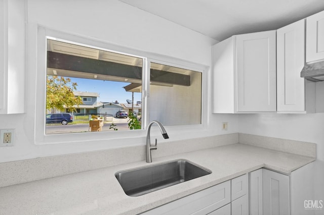 kitchen with light stone countertops, exhaust hood, white cabinetry, and sink