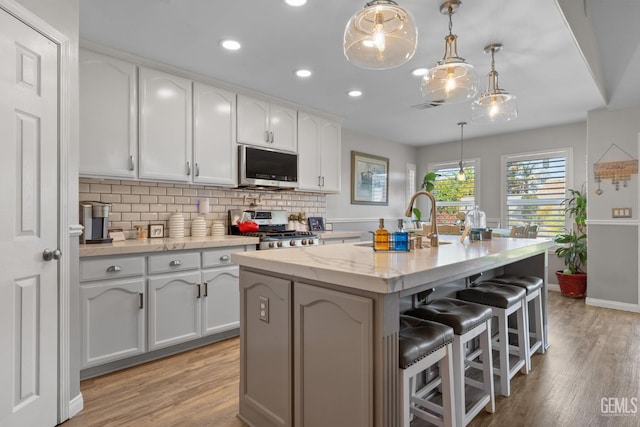 5512 Sicily Ct, Bakersfield, CA 93308 - kitchen with appliances with stainless steel finishes, light wood-style floors, backsplash, a kitchen breakfast bar, and recessed lighting