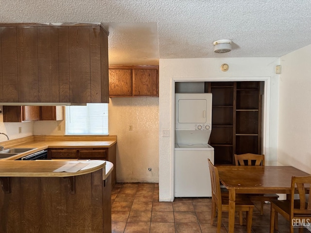 kitchen featuring a textured ceiling, kitchen peninsula, sink, and stacked washer and clothes dryer