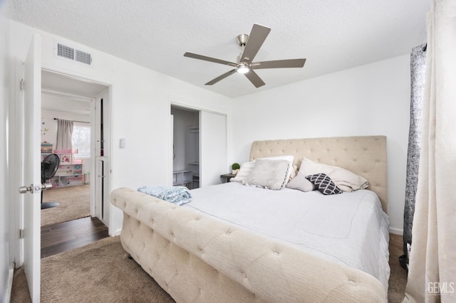 bedroom with ceiling fan, dark hardwood / wood-style floors, a textured ceiling, and a closet