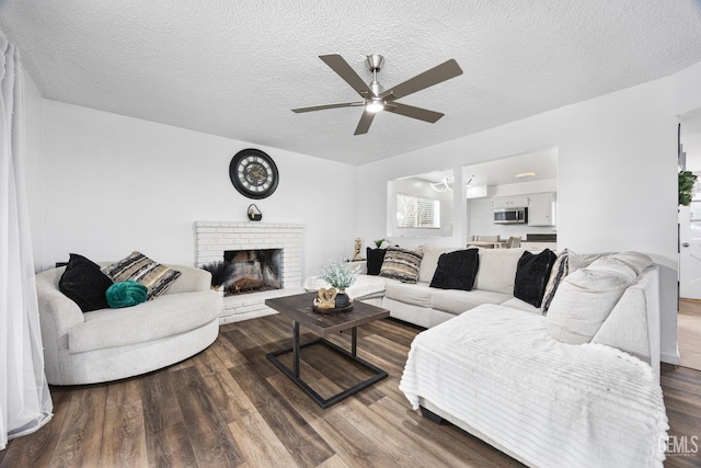 living room with a brick fireplace, ceiling fan, wood-type flooring, and a textured ceiling