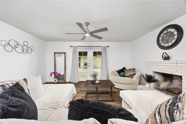 living room featuring wood-type flooring, french doors, a textured ceiling, ceiling fan, and a fireplace