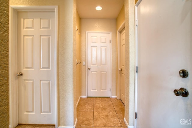 hall featuring light tile patterned floors, baseboards, and a textured wall