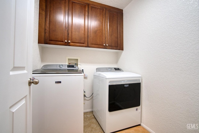 washroom featuring cabinet space, a textured wall, and separate washer and dryer