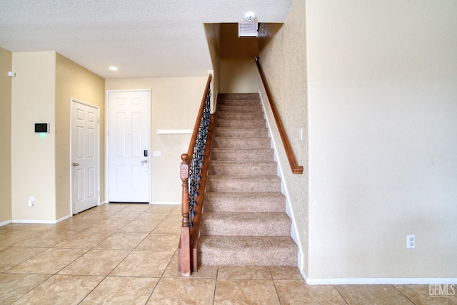 staircase with a textured ceiling, tile patterned flooring, and baseboards