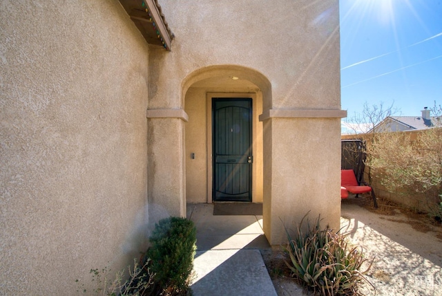 view of exterior entry with fence and stucco siding