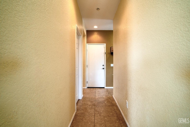 corridor with a textured wall, tile patterned flooring, and baseboards