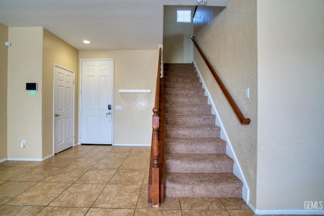 stairway featuring a textured ceiling, tile patterned flooring, and baseboards