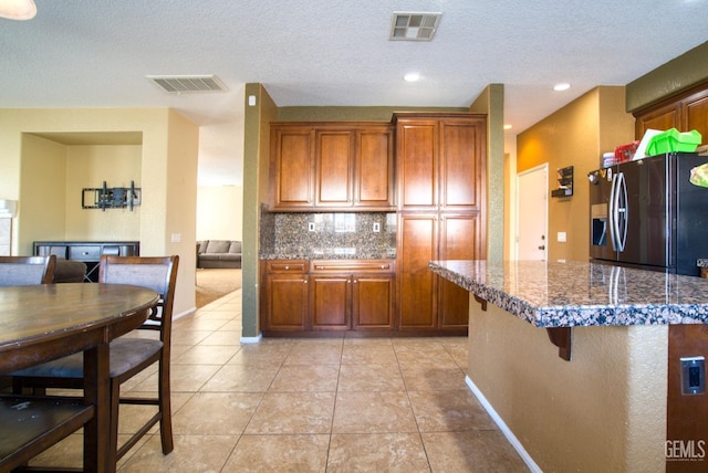 kitchen featuring tasteful backsplash, a breakfast bar, brown cabinetry, and visible vents