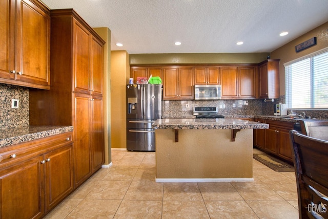 kitchen featuring a center island, appliances with stainless steel finishes, light tile patterned flooring, dark stone counters, and a kitchen breakfast bar