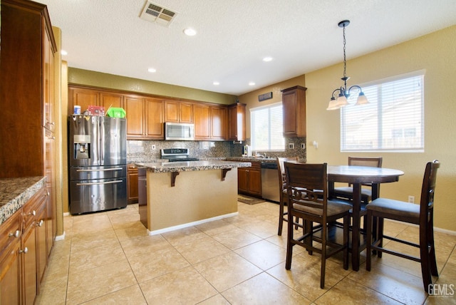 kitchen featuring visible vents, appliances with stainless steel finishes, a kitchen breakfast bar, light stone counters, and a center island