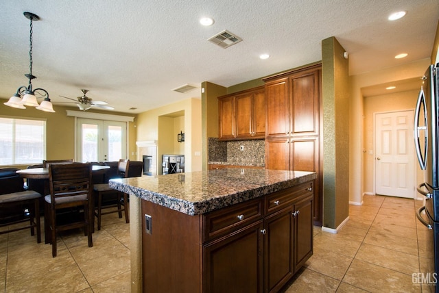 kitchen with visible vents, dark stone counters, freestanding refrigerator, a center island, and a textured ceiling