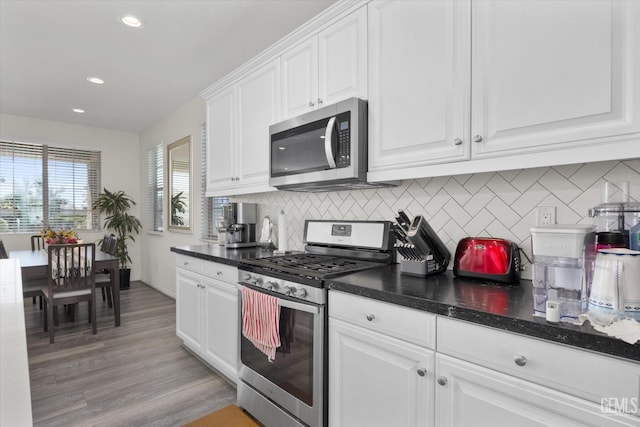 kitchen with tasteful backsplash, white cabinetry, stainless steel appliances, and dark countertops