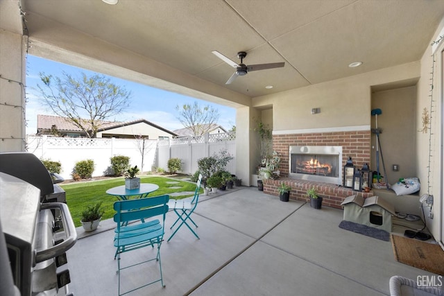 view of patio / terrace with a grill, a fenced backyard, a ceiling fan, and an outdoor brick fireplace