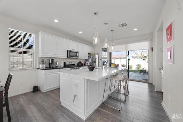 kitchen with visible vents, an island with sink, stainless steel appliances, white cabinets, and backsplash