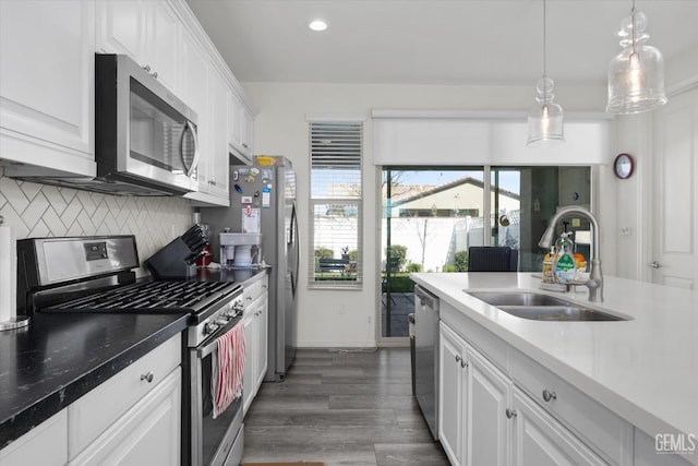 kitchen with dark wood finished floors, a sink, decorative backsplash, appliances with stainless steel finishes, and white cabinetry