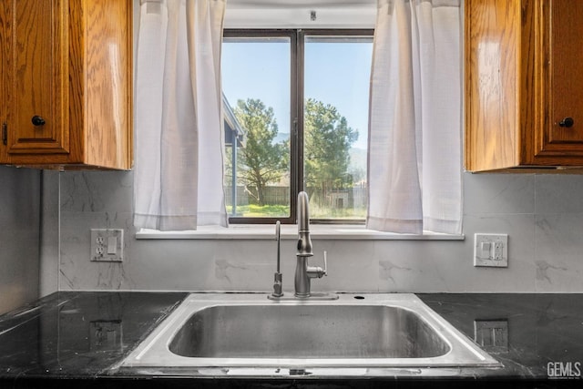 kitchen with brown cabinets, dark countertops, a sink, and a healthy amount of sunlight