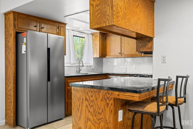 kitchen with decorative backsplash, brown cabinetry, dark countertops, a sink, and freestanding refrigerator