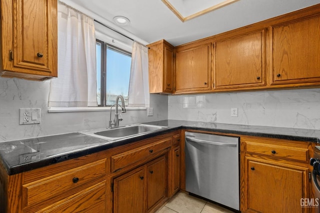 kitchen with brown cabinetry, backsplash, dark countertops, stainless steel dishwasher, and a sink