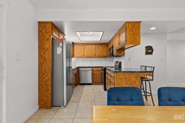 kitchen featuring dark countertops, a breakfast bar, brown cabinetry, baseboards, and black appliances