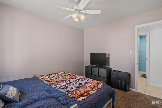 bedroom featuring a ceiling fan, baseboards, light carpet, and light tile patterned floors